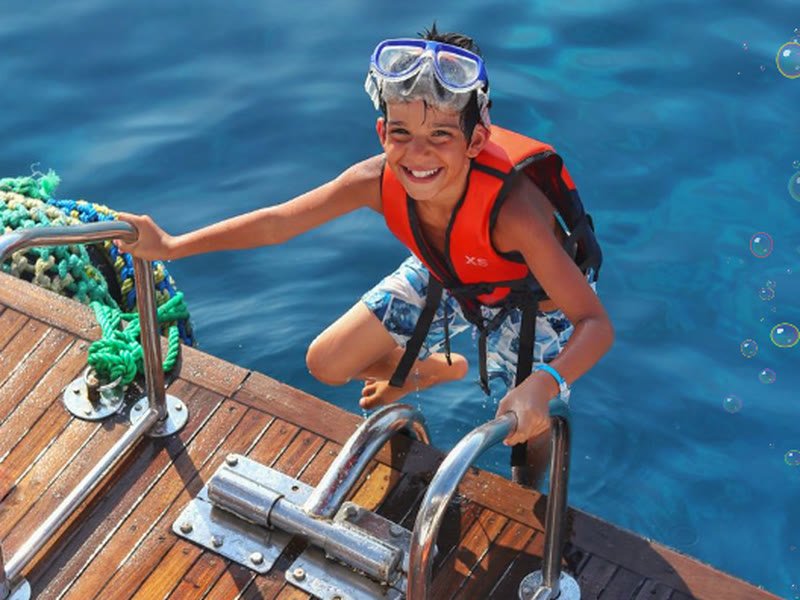 Kind mit Tauchmaske und Schwimmweste an der Bootsleiter